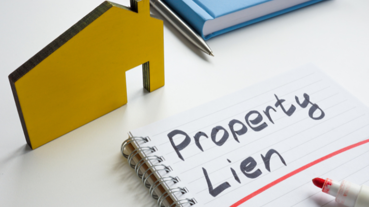 A small house cutout and a notebook with the words 'property lien' written on it on top of a white table.