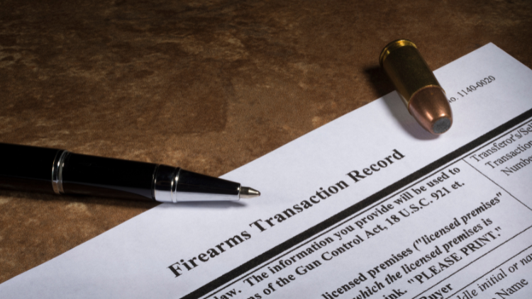 Close-up view of a firearms transaction record form with a pen and a bullet on top.