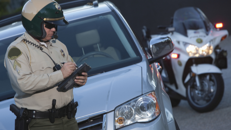 Eye-level view of a traffic police officer in front of a car writing a ticket.